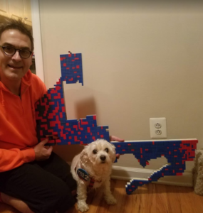 Kevin Deegan-Krause kneels next to his dog and holds up his scale model of the old 14th Congressional District, made entirely out of Lego.