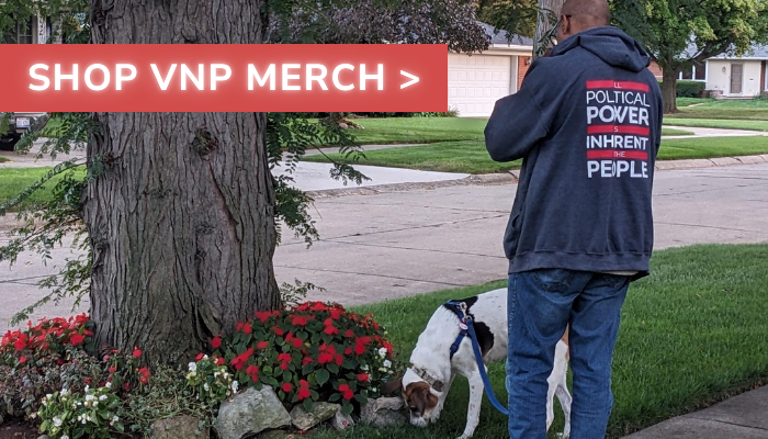 Person in a hoodie (Hoodie Text: All Political Power is Inherent in the People) walking a dog by a tree with flowers, with a banner reading "SHOP VNP MERCH".