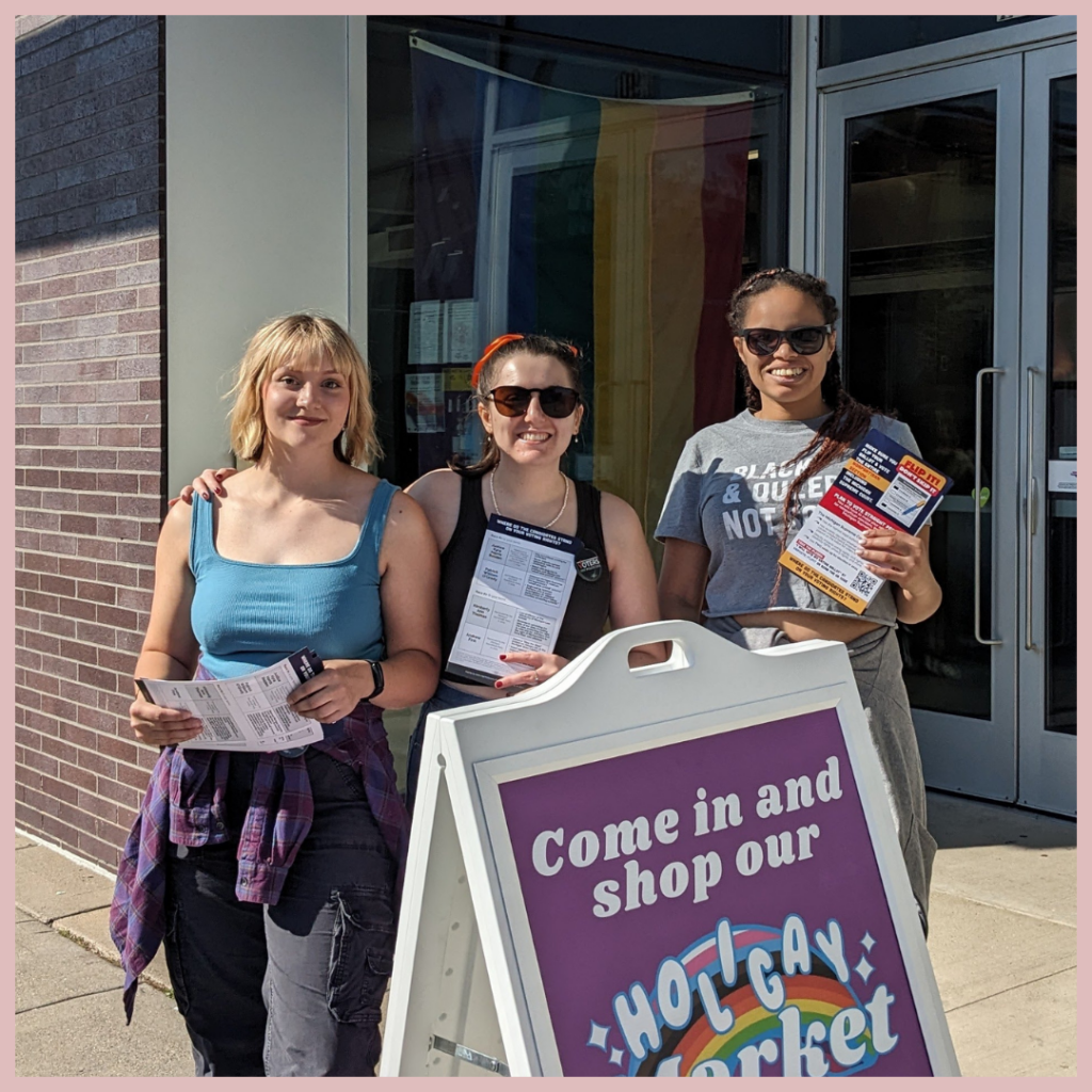 Three people standing outside with flyers next to a sign that reads "Come in and shop our Holigay Market."