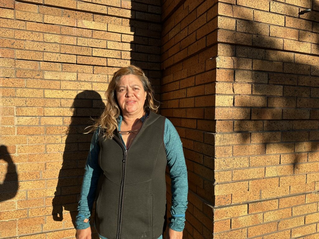 Woman standing in front of a sunlit brick wall.